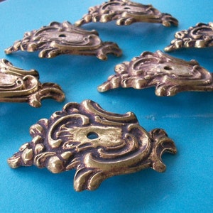 May include: Six ornate brass decorative accents with intricate floral designs. Each accent has a hole in the center.