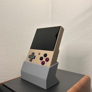 Miyoo Mini plus handheld gaming device shown in the gray dock, showing the aesthetic angle from the side.