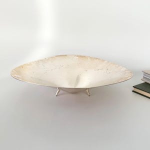 Puede incluir: Una taza de cerámica blanca con un asa negra y el texto "But First, Coffee" en un estilo manuscrito. La taza está sobre una superficie blanca. La taza mide aproximadamente 10 cm de alto.