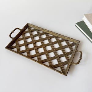 May include: A rectangular brass tray with a lattice design. The tray features two curved handles and a decorative border. The openwork pattern allows the surface beneath to be seen. Likely used for serving or display, it has a vintage aesthetic.