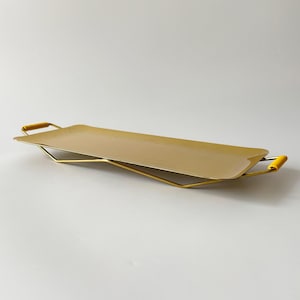 May include: A rectangular, matte gold serving tray with a smooth, flat surface. The tray features a thin, gold-toned metal wire frame base and two small, bright yellow cylindrical handles on each end for easy lifting and carrying.
