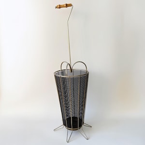 Puede incluir: Un paragüero vintage con cuerpo de malla negra y estructura metálica. El soporte tiene un asa de bambú y un diseño único, perfecto para guardar paraguas. El soporte mide aproximadamente 71 cm de alto.
