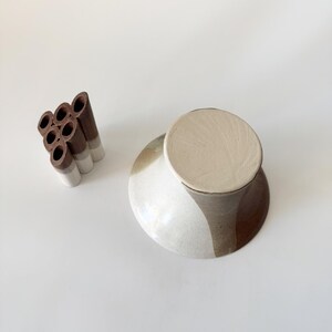 May include: A ceramic vase with a brown and white glaze. The vase has a wide, round base and a narrow neck. The vase is designed to hold multiple stems of flowers.