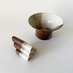 May include: A brown and white ceramic bowl with a flared rim and a stack of brown and white ceramic tubes with holes.