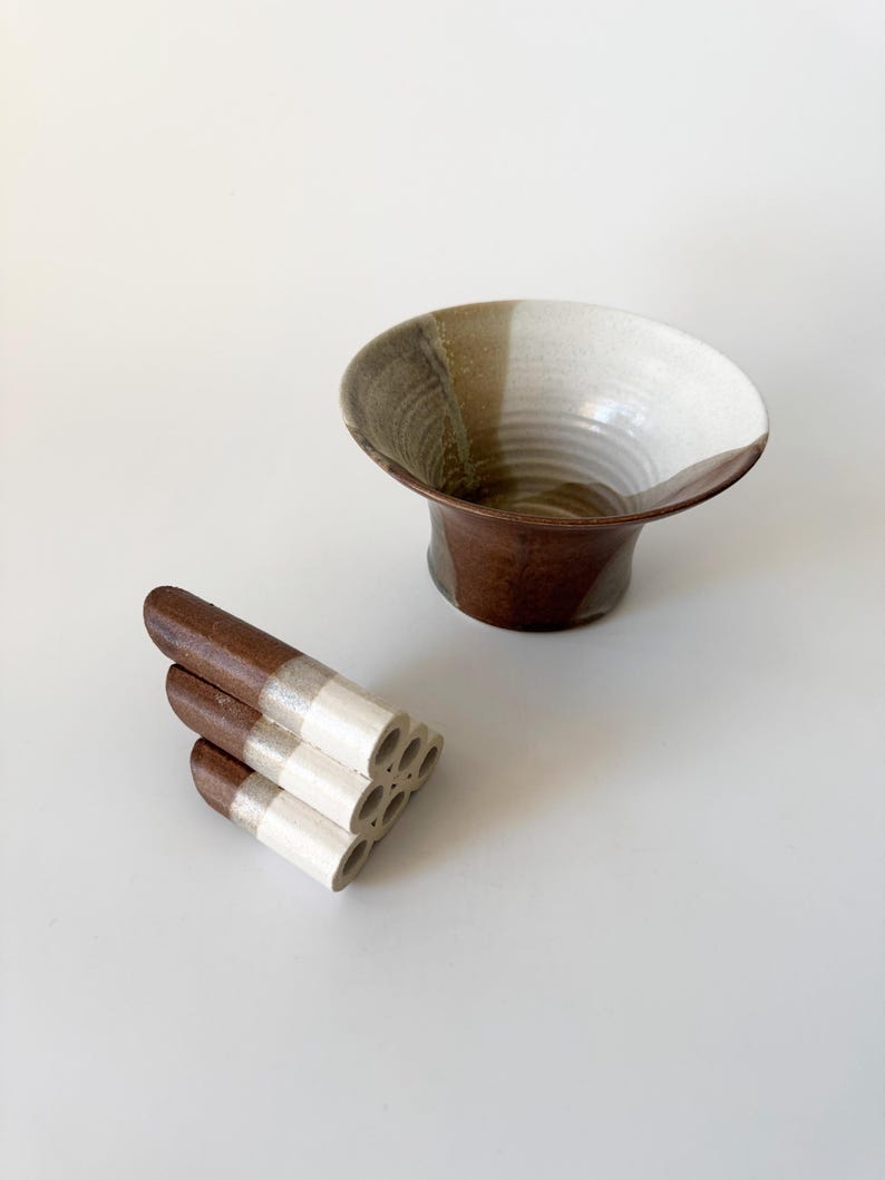 May include: A brown and white ceramic bowl with a flared rim and a stack of brown and white ceramic tubes with holes.