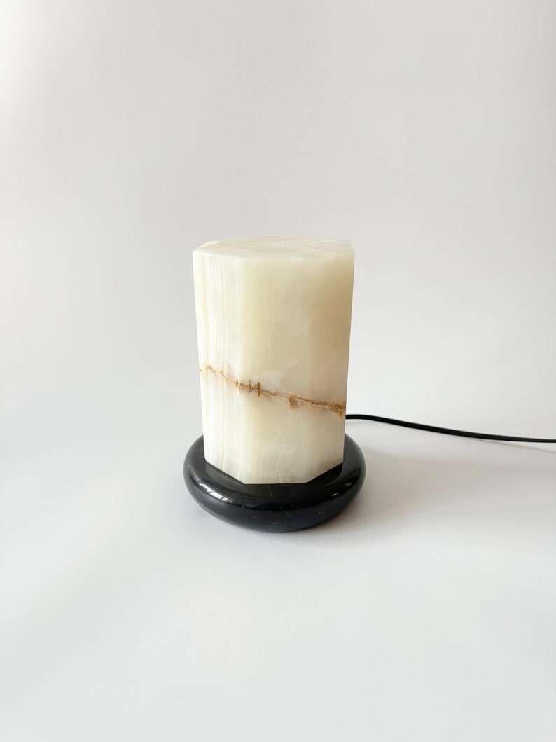 May include: A white alabaster lamp with a black base. The lamp has a geometric shape and a natural, veined pattern.