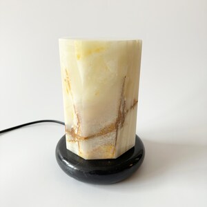 May include: A white onyx lamp with a black marble base. The lamp has a geometric shape and features natural veining.