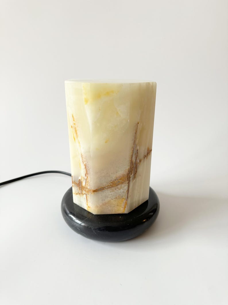 May include: A white onyx lamp with a black marble base. The lamp has a geometric shape and features natural veining.