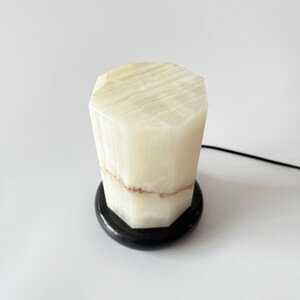 May include: A white onyx lamp with a black marble base. The lamp has a geometric shape and a natural, striated pattern.