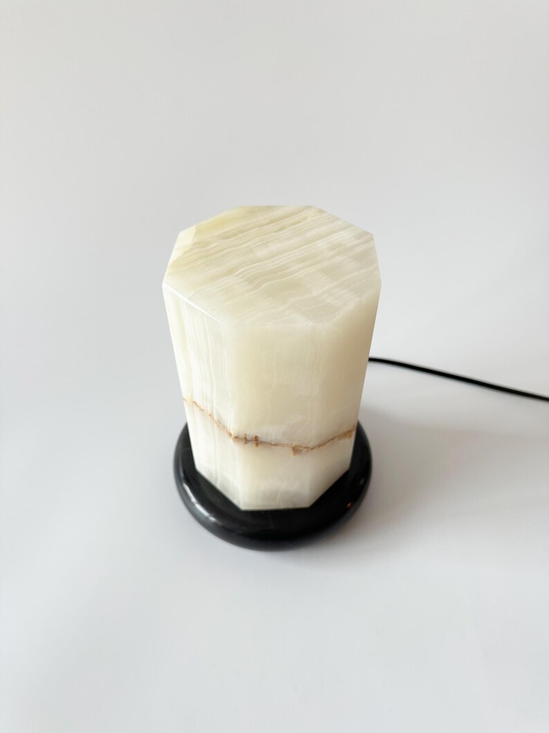 May include: A white onyx lamp with a black marble base. The lamp has a geometric shape and a natural, striated pattern.