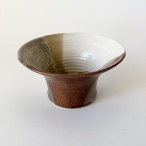 May include: A brown, white, and green ceramic bowl with a flared rim and a rounded base. The bowl has a unique glaze pattern.