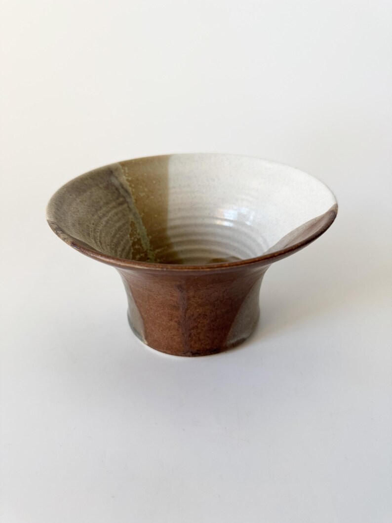 May include: A brown, white, and green ceramic bowl with a flared rim and a rounded base. The bowl has a unique glaze pattern.