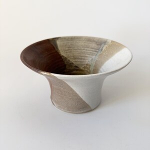May include: A ceramic vase with a wide, flared opening and a narrow base. The vase is decorated with a swirling pattern of brown, white, and beige glaze.