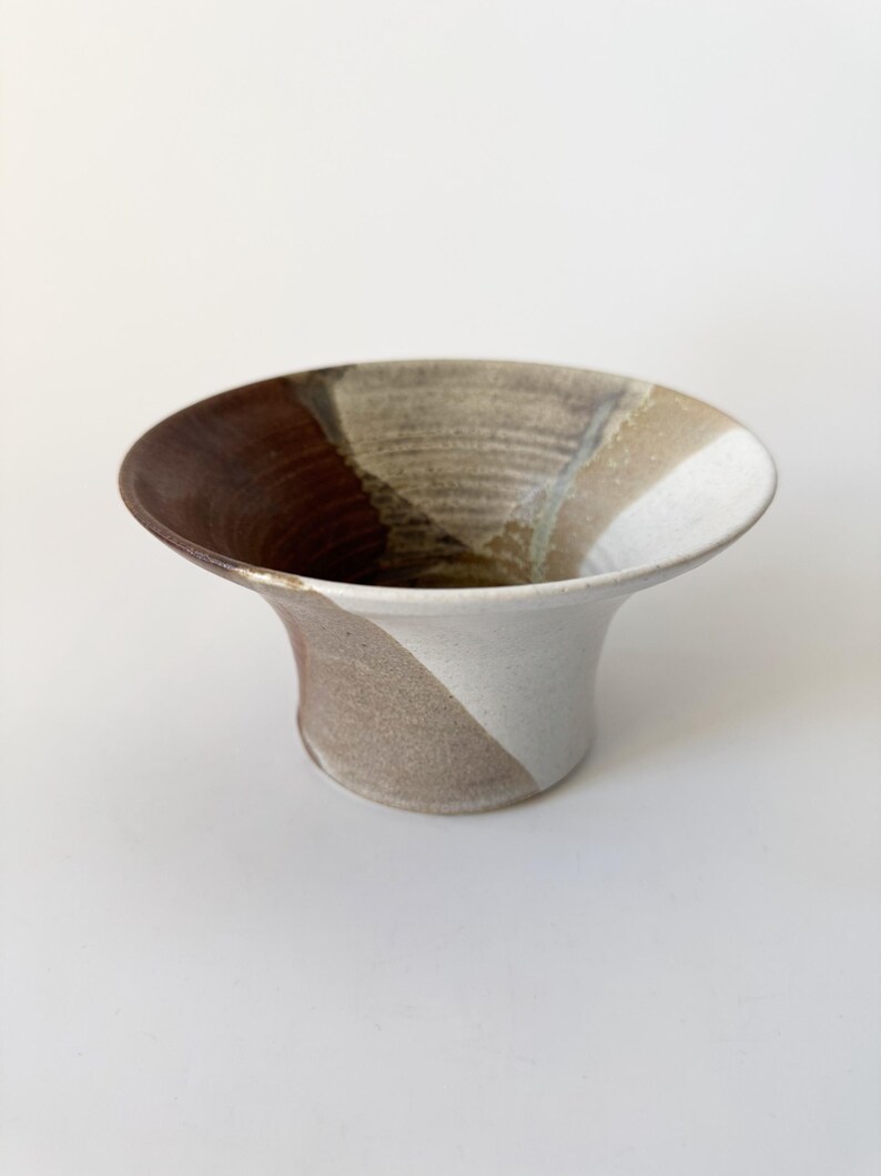 May include: A ceramic vase with a wide, flared opening and a narrow base. The vase is decorated with a swirling pattern of brown, white, and beige glaze.