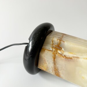 May include: A white and brown onyx lamp base with a black marble base. The lamp base is cylindrical and has a smooth, polished finish.