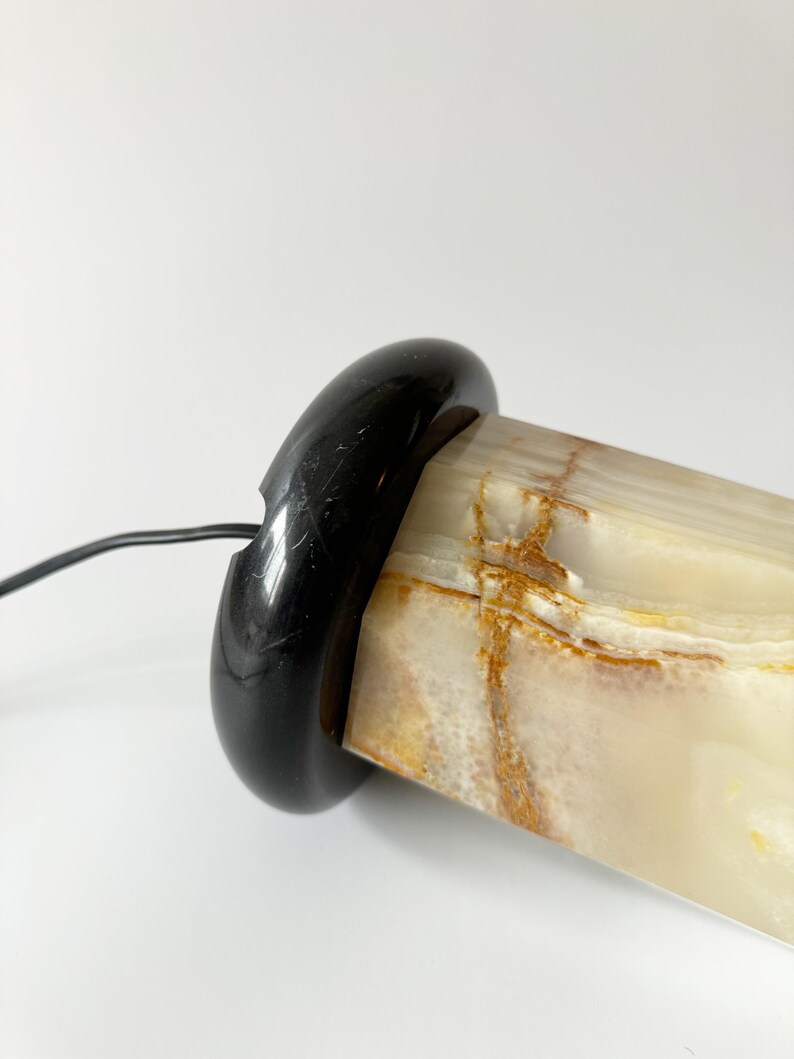 May include: A white and brown onyx lamp base with a black marble base. The lamp base is cylindrical and has a smooth, polished finish.