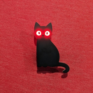 May include: A black cat-shaped object with glowing red eyes. The cat is sitting with its tail curled. The background is a solid red color.