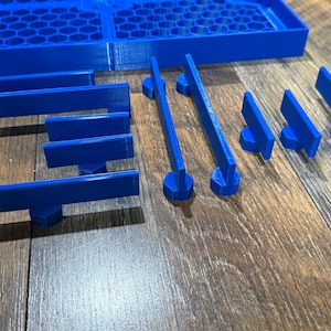 Puede incluir: Un conjunto de piezas de juego de pl&aacute;stico azul, que incluyen piezas rectangulares largas y piezas m&aacute;s cortas con un extremo redondeado. Las piezas est&aacute;n dispuestas sobre una superficie de madera.