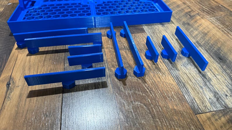 Puede incluir: Un conjunto de piezas de juego de pl&aacute;stico azul, que incluyen piezas rectangulares largas y piezas m&aacute;s cortas con un extremo redondeado. Las piezas est&aacute;n dispuestas sobre una superficie de madera.