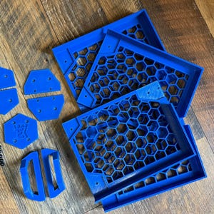 Puede incluir: Un conjunto de piezas impresas en 3D de color azul para una caja de ordenador. Las piezas incluyen un panel en forma de panal, un panel rectangular y varias piezas m&aacute;s peque&ntilde;as. Tambi&eacute;n se incluyen peque&ntilde;os tornillos negros.