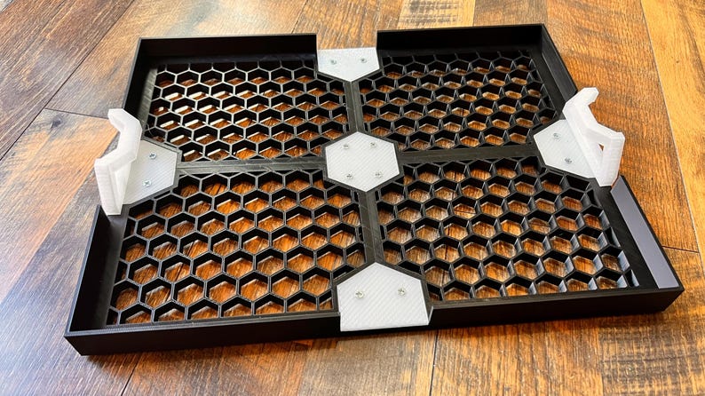 Puede incluir: Cuatro baldosas cuadradas negras con un patr&oacute;n de panal y conectores de pl&aacute;stico blanco. Las baldosas est&aacute;n dispuestas en forma de cuadrado.