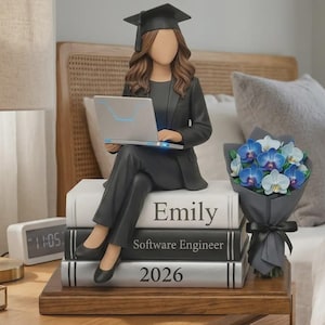 Könnte beinhalten: Eine Abschlussfigur einer Frau in Hut und Robe, die auf Büchern mit der Aufschrift "Emily", "Software Engineer" und "2026" sitzt und einen Laptop hält. Ein Strauß blauer und weißer Blumen steht daneben. Die Figur steht auf einem Nachttisch aus Holz.