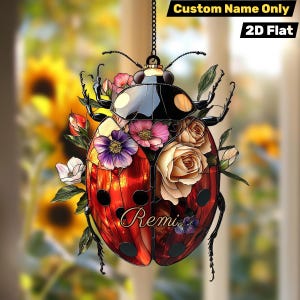 Può includere: Un ornamento decorativo a forma di coccinella con corpo rosso e nero, adornato con fiori colorati. L'ornamento è sospeso da una catena e presenta il nome "Remi". Il testo "Custom Name Only" e "2D Flat" sono anch'essi visibili.