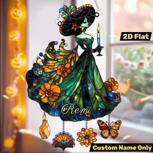 May include: A stained glass suncatcher depicting a woman in a wide-brimmed hat and gown, holding a candle. The design incorporates orange, green, and blue floral and butterfly accents. The text "Remi" is displayed on the gown, with "Custom Name Only" below.