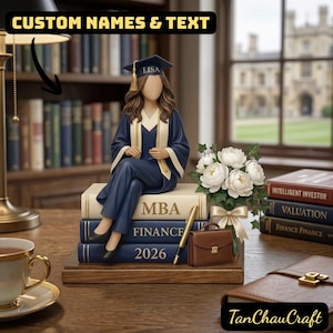 Puede incluir: Figura de graduación de una persona con birrete y toga azules, sentada sobre libros con la etiqueta "MBA FINANCE 2026". La figura tiene el nombre "LISA" en el birrete. También hay un ramo de flores blancas y un maletín marrón. El texto "CUSTOM NAMES & TEXT" está en la parte superior.