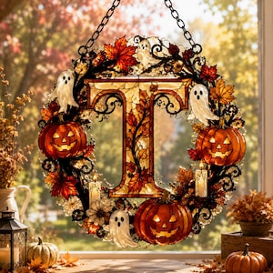 May include: A circular decorative wreath featuring a central letter T, surrounded by orange jack-o'-lanterns, white ghost figures, and autumn-colored maple leaves. The design includes small lit candles and black metal scrollwork, suspended by a chain.