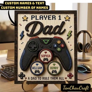 Op de afbeelding: Houten bord met een zwart frame met een videogamecontroller-ontwerp. Het bord zegt "PLAYER 1 Dad" met aanpasbare naamcirkels. De tekst "A DAD TO RULE THEM ALL" is inbegrepen.