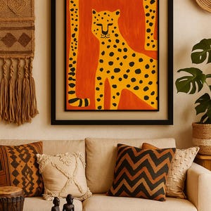 Pode incluir: Uma impressão artística emoldurada com um guepardo amarelo com manchas pretas sobre um fundo laranja. A obra de arte é exibida acima de um sofá bege com almofadas decorativas. O quarto é decorado em tons quentes e terrosos.
