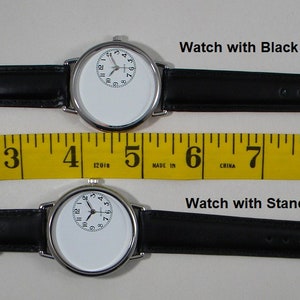 May include: Two silver-tone wristwatches with black bands and white faces featuring an off-center clock dial. A yellow measuring tape shows the top watch with a long band measures 10 inches and the bottom watch with a standard band measures 9 inches.