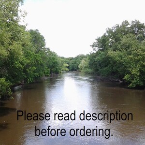 May include: A view of a river flowing through a wooded area. The river is calm and the water is brown. The trees on either side of the river are green and lush. The sky is overcast and the sun is not visible. The text "Please read description before ordering." is visible in the lower part of the image.