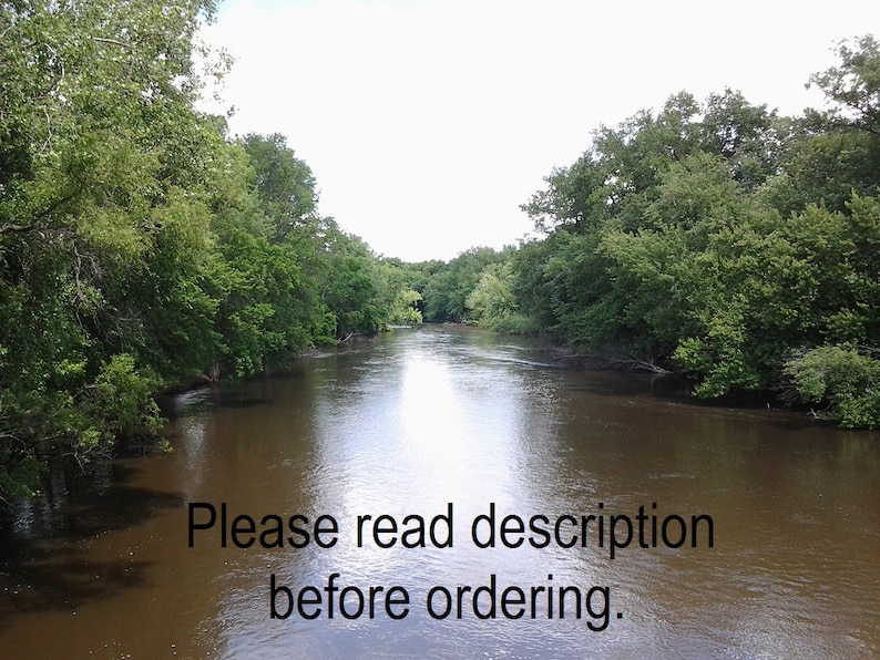 May include: A view of a river flowing through a wooded area. The river is calm and the water is brown. The trees on either side of the river are green and lush. The sky is overcast and the sun is not visible. The text "Please read description before ordering." is visible in the lower part of the image.