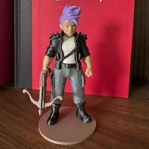 May include: A figurine of a character with purple hair, wearing a black jacket with spikes, gray pants, and black boots, holding a crossbow. The figure stands on a brown circular base in front of a red backdrop with a silver anarchy symbol.