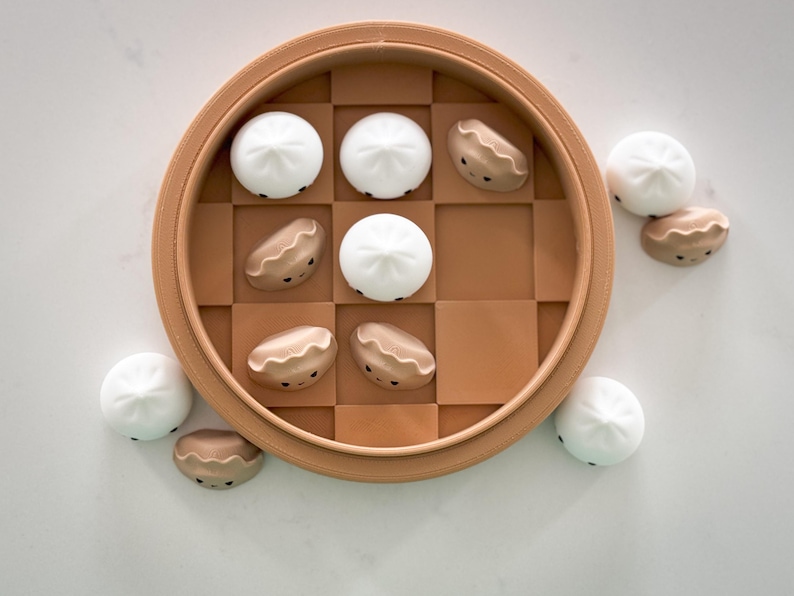 May include: A brown wooden board game with a chequered pattern. The board game is filled with small white and brown dumplings with faces. There are also several dumplings outside of the board game.