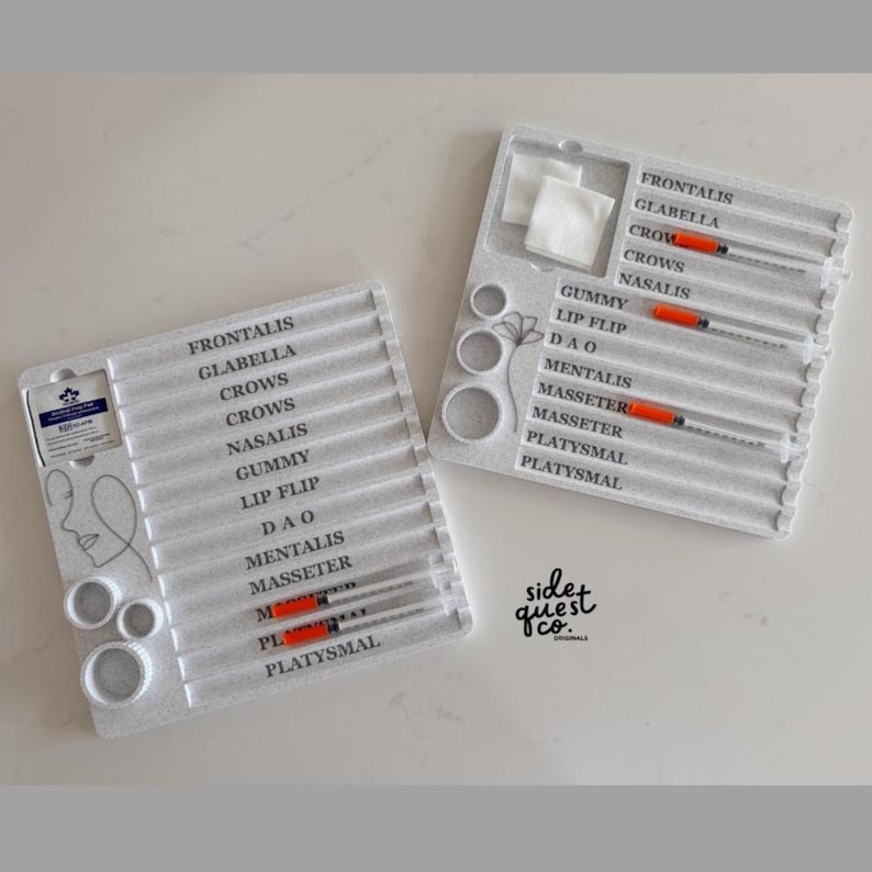 May include: Two white trays with labels and syringes, likely for cosmetic procedures. Each tray has multiple labeled slots, including "Frontalis," "Glabella," and "Crows." The syringes have orange plungers. The trays also include cotton pads and circular containers.