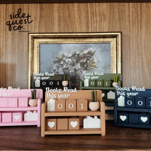 May include: Wooden bookshelf-style book counters in pink, natural, green, and navy blue. Each shelf displays the text "Books Read this year" and has blocks to track the number of books read. The counters also feature small potted plants and heart-shaped details.