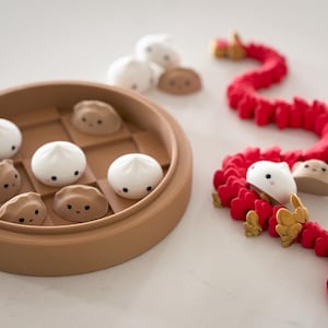 May include: A brown and white dim sum game with a red and gold dragon. The game includes a brown steamer basket with white dim sum pieces and a red dragon with gold accents.
