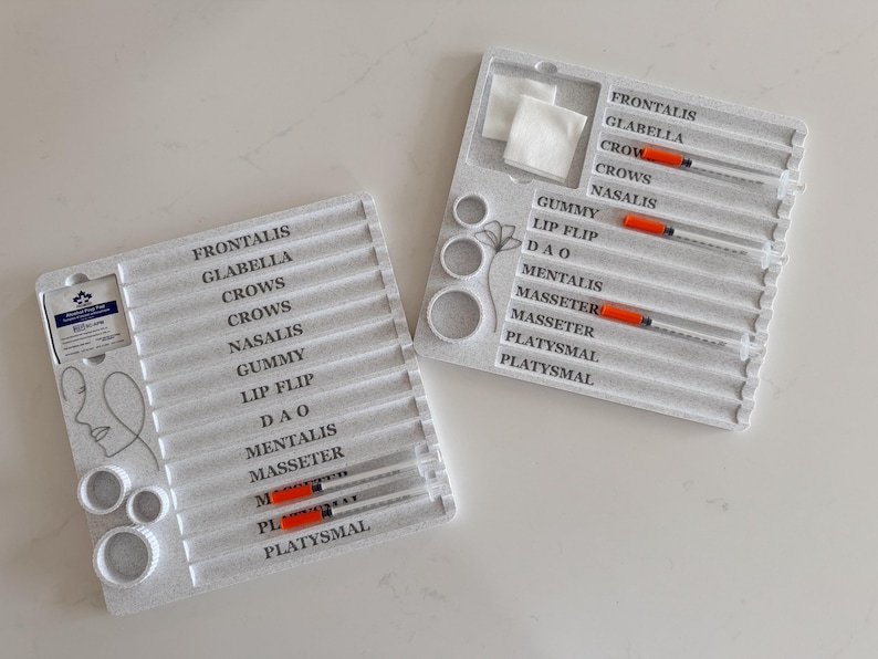 May include: Two white plastic trays with syringes and labels for cosmetic procedures. The labels include terms like "Frontalis," "Glabella," and "Masseter." Each tray has multiple syringes with orange plungers and a section for cotton pads.