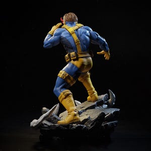 May include: A detailed figurine of the X-Men character Cyclops, in a dynamic pose. The figure is clad in a blue and yellow costume, with a red visor. The statue is standing on a rocky base, with a black background.
