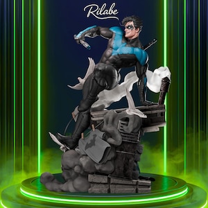 May include: A detailed statue of Nightwing in a dynamic pose, clad in a black and blue costume. The figure is set on a detailed base with a gray Batman t-shirt hanging on a clothesline. The background is a gradient of blue and green with the "Rilabe" logo.