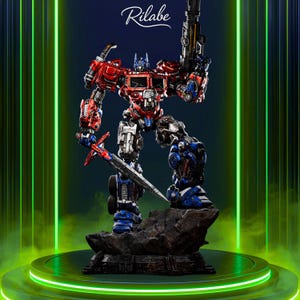 May include: A detailed Optimus Prime action figure, primarily red, blue, and silver, holding a sword and a blaster. The figure is posed on a rocky base, with the word "Rilabe" in script above. The background features green neon lights.