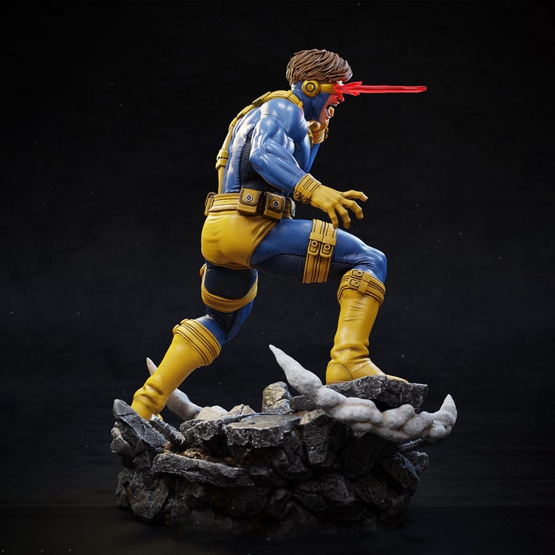 May include: A detailed figurine of a superhero in a dynamic pose, wearing a blue and yellow costume. The figure has a red beam emanating from its eyes, and is standing on a rocky base. The figure is approximately 12 inches tall.