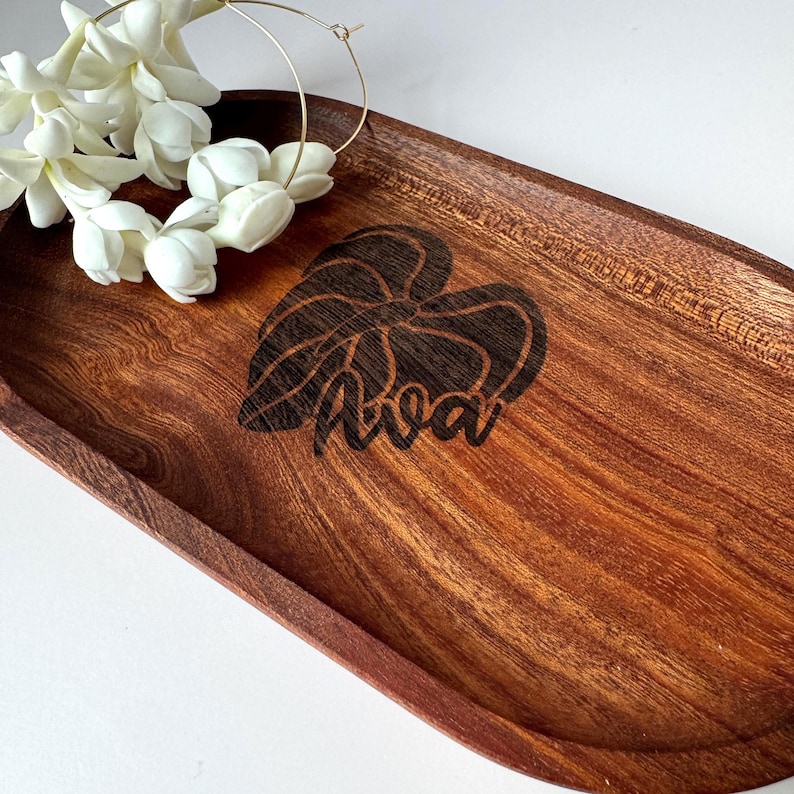 May include: A wooden serving tray with a dark brown finish. The tray features a laser-etched design of a leaf and the name "Ava". White flowers and a gold hoop earring are placed on the tray.