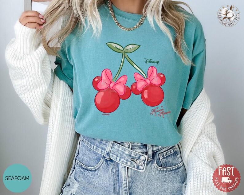 Peut inclure: T-shirt vert d'eau avec un motif de cerises de dessin anim&eacute;, des n&oelig;uds roses et le texte "Disney Minnie Mouse". Le t-shirt est fait d'une mati&egrave;re douce.