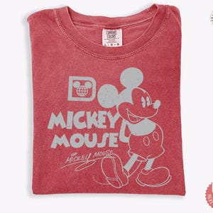 May include: Red t-shirt with a distressed Mickey Mouse graphic. The design includes Mickey's image, the words "Mickey Mouse," and a globe icon. The shirt is folded and has a Comfort Colors tag.
