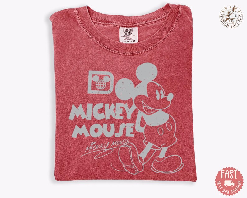 May include: Red t-shirt with a distressed Mickey Mouse graphic. The design includes Mickey's image, the words "Mickey Mouse," and a globe icon. The shirt is folded and has a Comfort Colors tag.