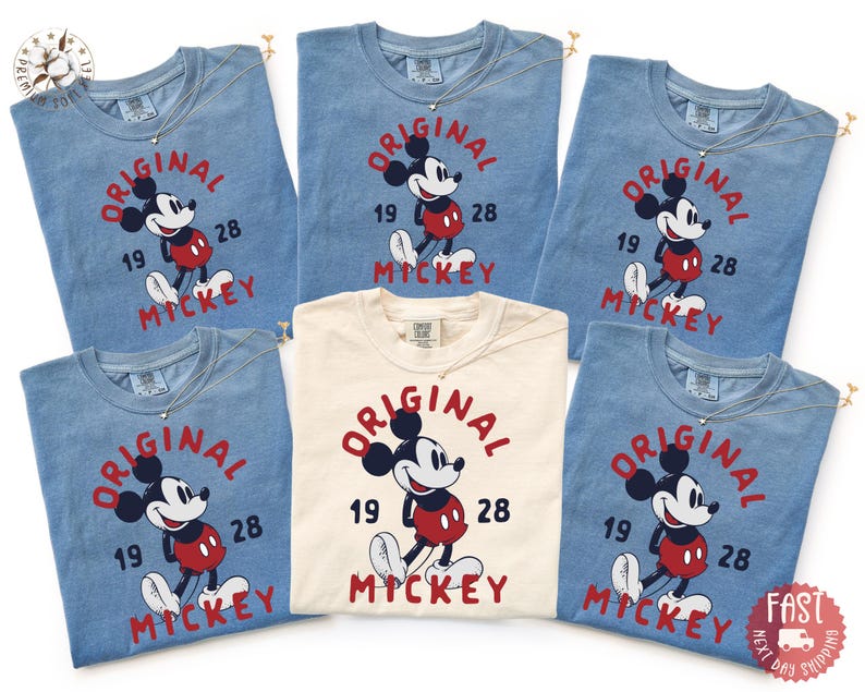 May include: A collection of blue and cream-colored t-shirts featuring a vintage-style Mickey Mouse graphic. The design includes the words "ORIGINAL," "MICKEY," and the numbers "19" and "28." Each shirt has a small silver necklace.